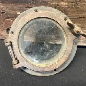 An old rusty Brass Porthole #10 on a wooden surface.