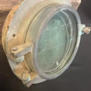 An old Brass Porthole # 10 on top of a piece of wood.