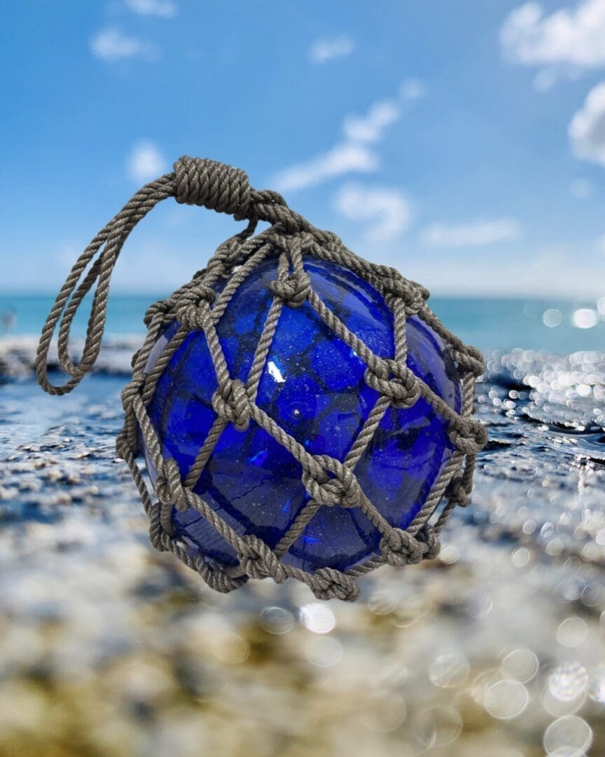 A blue glass ball with rope on the beach.