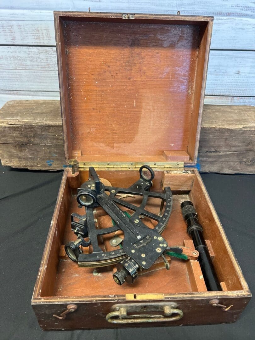 A wooden box with an old style sextant sitting on top of it.