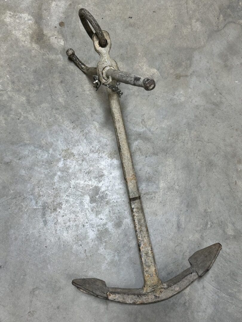 An old, rusty metal anchor lying on a concrete surface.