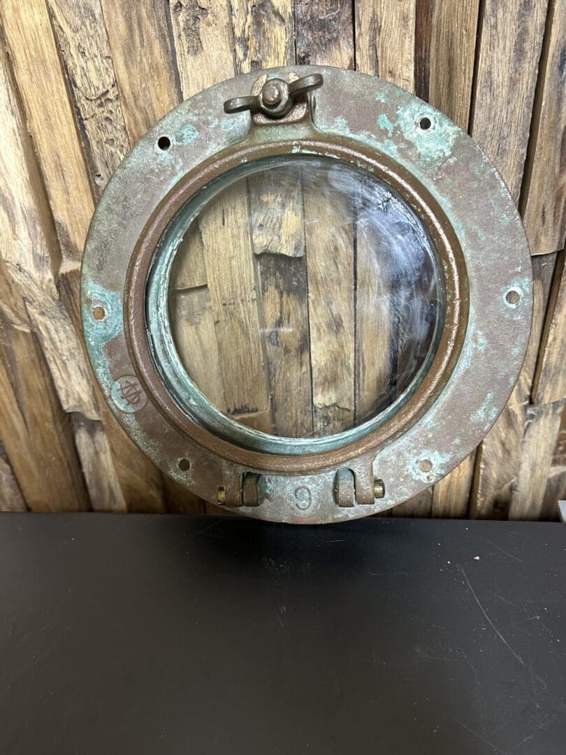 A vintage brass porthole window with green patina on a wooden background.