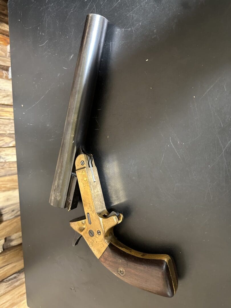 Vintage single-barrel flare gun with wooden handle on a dark surface.