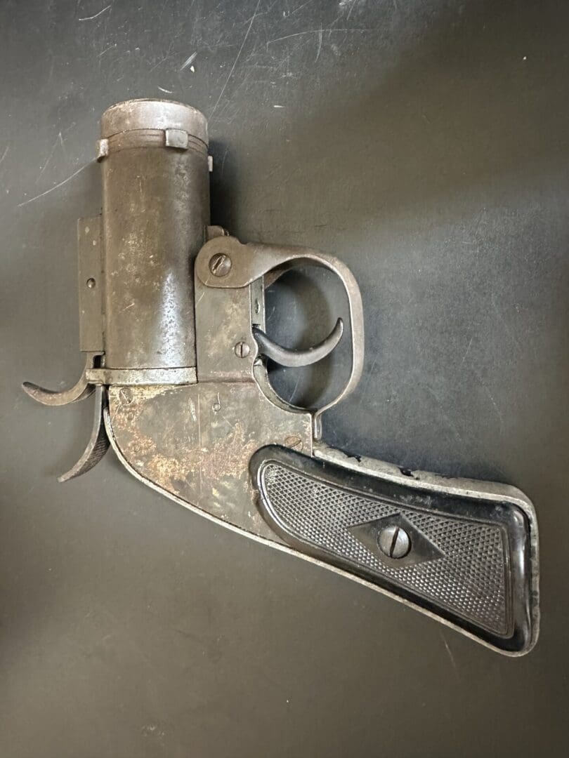 An old, rusty, single-shot flare gun with a black grip on a dark surface.
