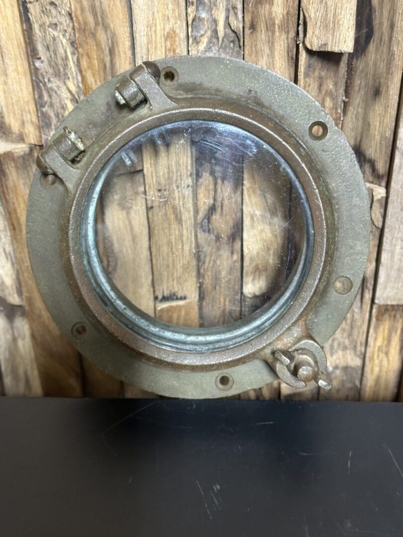 Rustic metal porthole window with glass and latch on wooden background.
