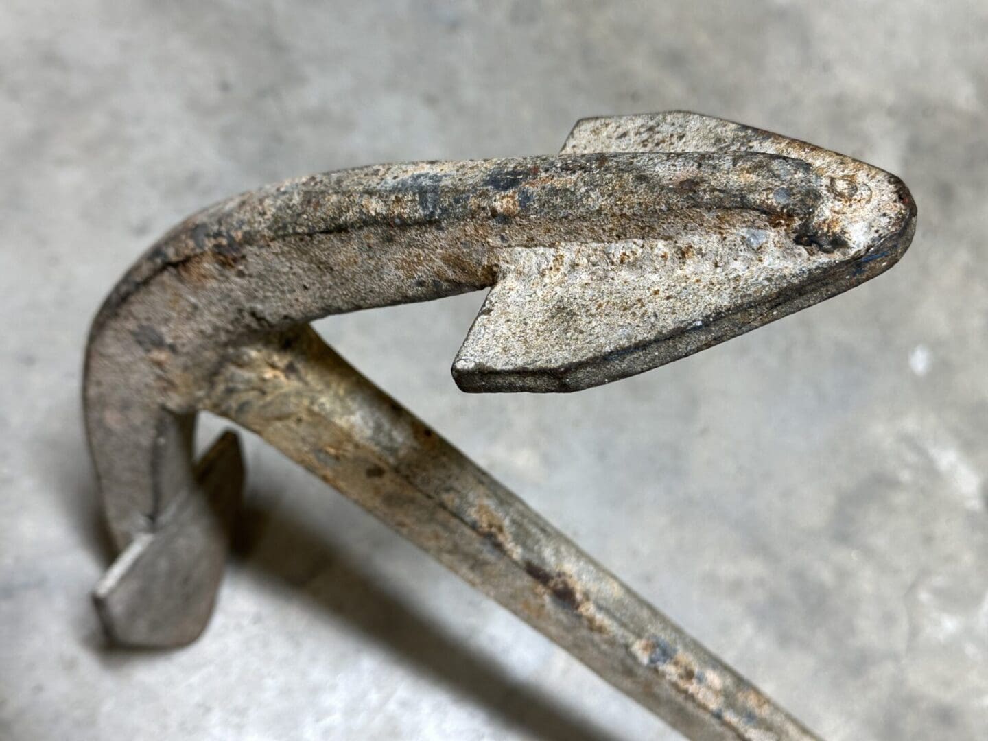 Close-up of a rusty metal hook with a pointed tip on a concrete surface.