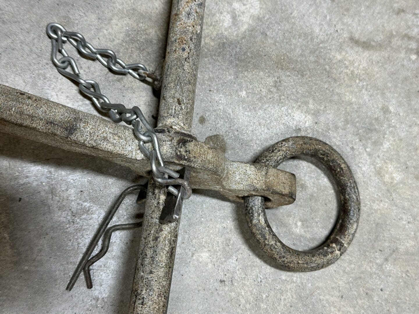 Close-up of a rusty metal ring and chain on a concrete floor.