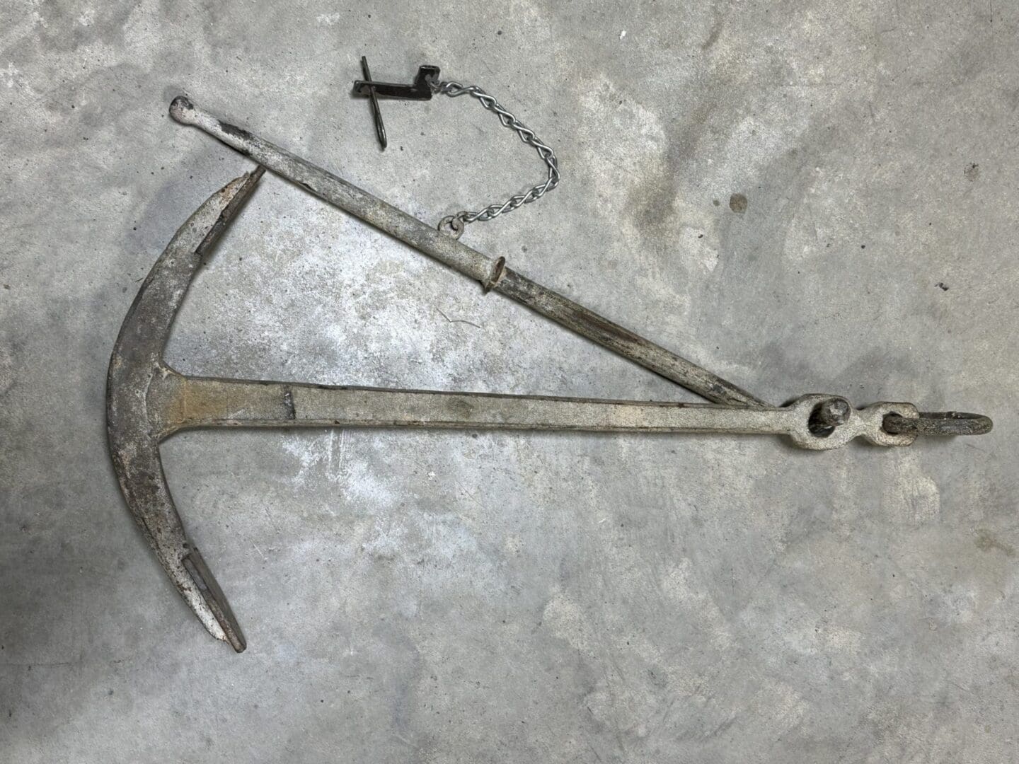 A weathered metal ship anchor lies on a concrete surface.