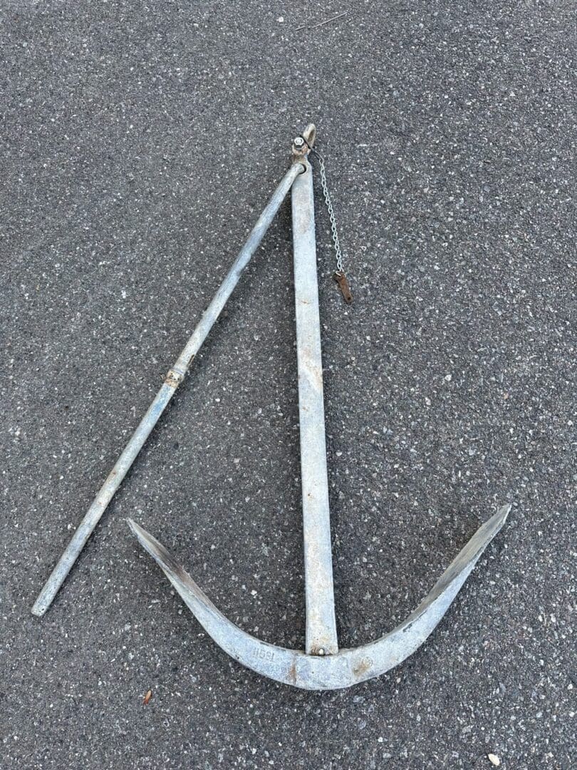 A metal anchor lying on asphalt ground.