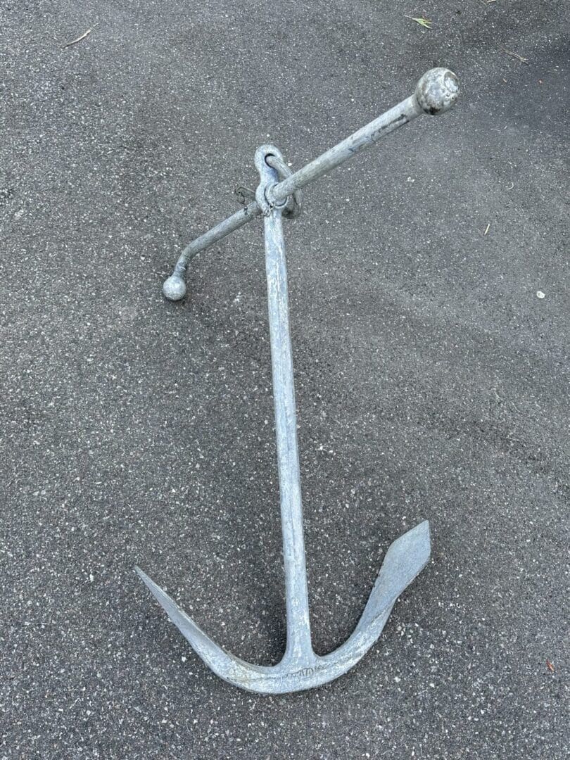 A large metal ship anchor resting on asphalt.
