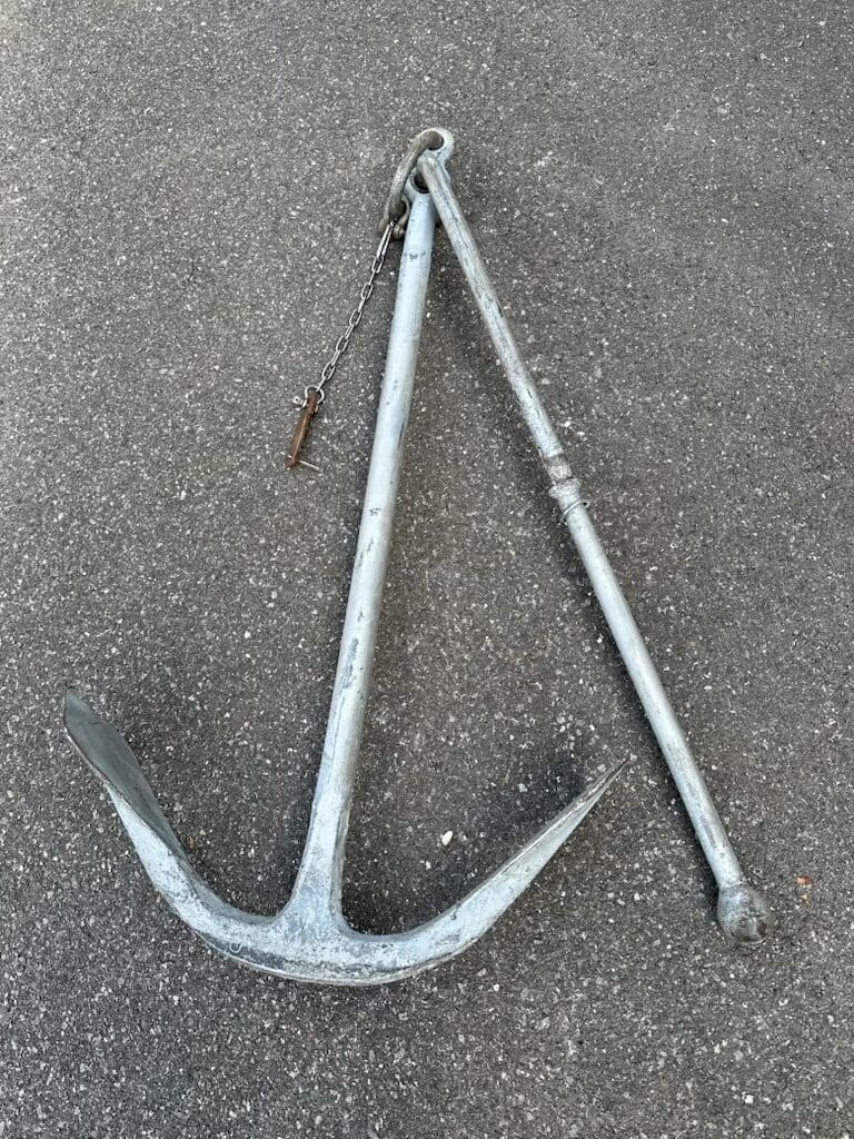 A metal ship anchor with a chain, lying on asphalt.