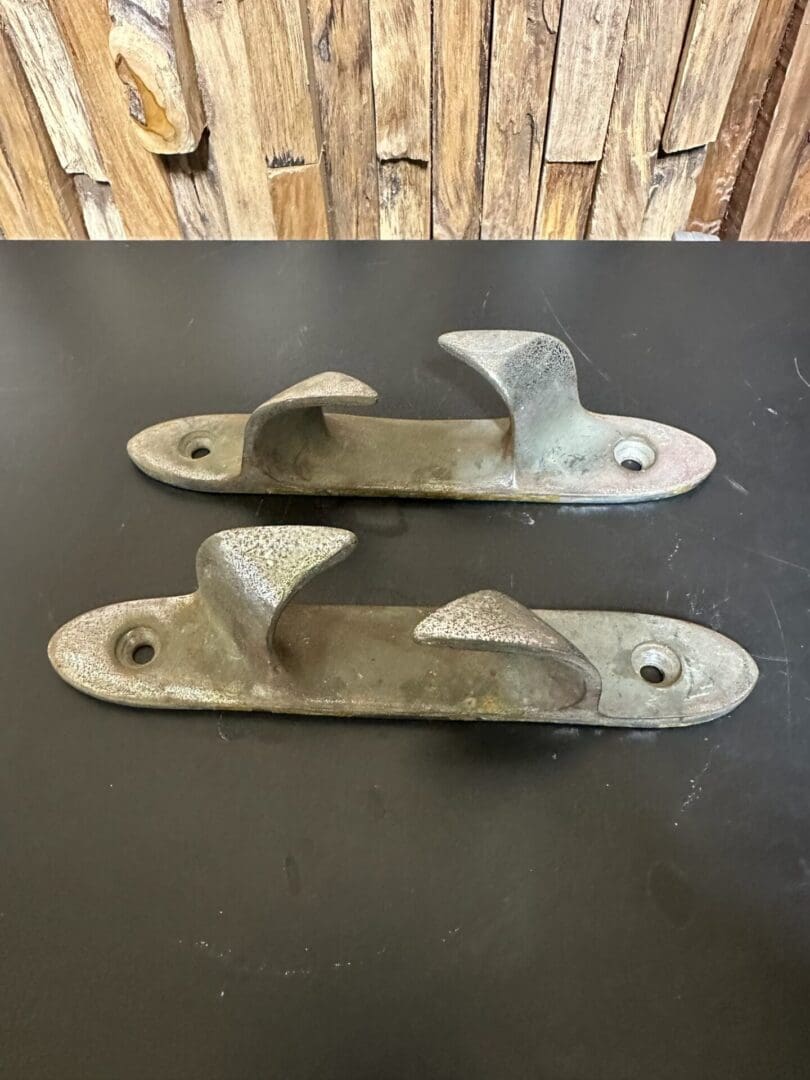 Two metal boat cleats on a black surface with a wooden background.