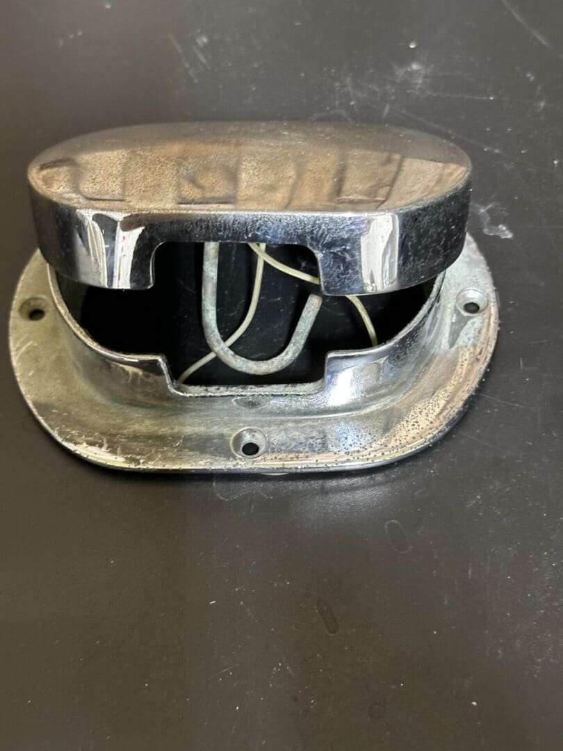 Old metallic electrical fixture with exposed wires and screws on a dark surface.