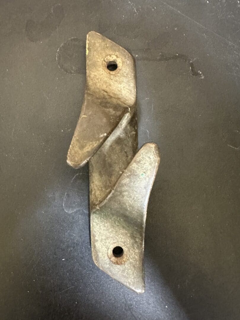 Rusty metal bracket with two screw holes on a dark surface.