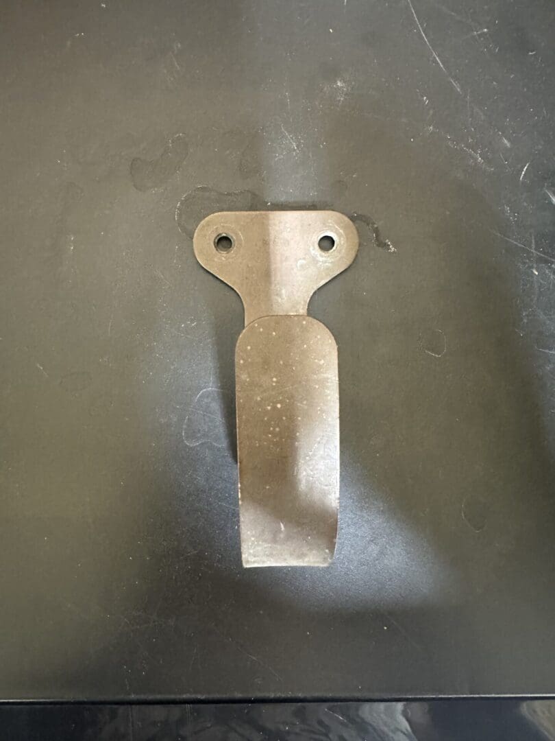 Rusty metal clip with two mounting holes on a dark surface.