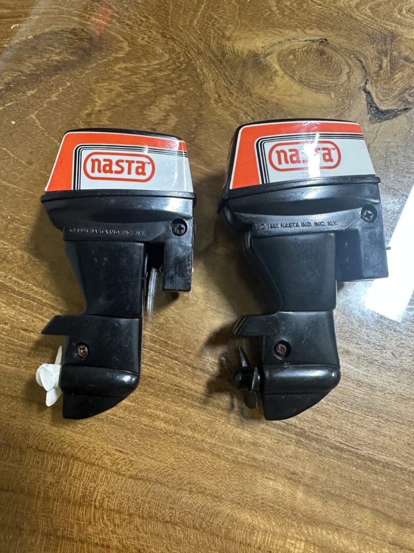Two vintage Nasta toy outboard motors on a wooden surface.