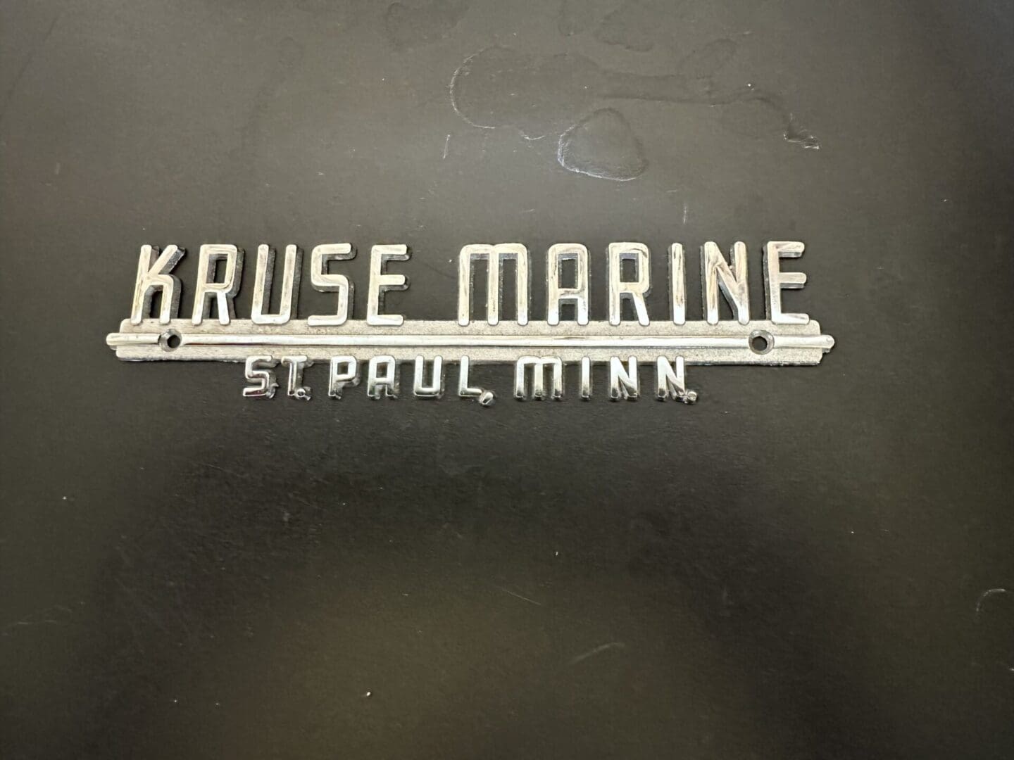 Metal badge reading 'Kruse Marine St. Paul, Minn.' on a black background.